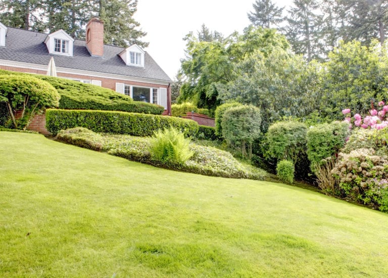Brick red house with English garden and white window shutters. Summer landscape.